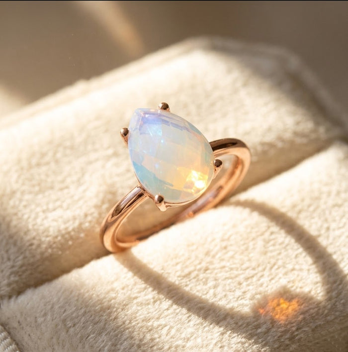 Rose gold opalite teardrop prong ring shown in warm light, a soft iridescent October birthstone ring with a faceted pear gemstone.