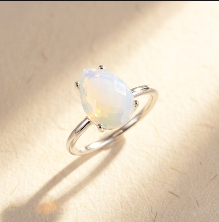 Sterling silver opalite teardrop ring shown on fabric, a dainty October birthstone ring with a pear-shaped gemstone and prong setting.