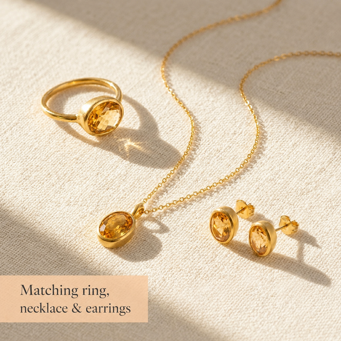 Matching citrine ring, necklace, and earrings set in gold with oval faceted gemstones on a warm cream background.