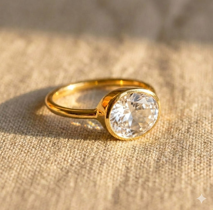 Oval clear quartz ring in gold bezel setting on linen, minimalist gemstone ring for women