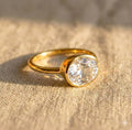 Oval clear quartz ring in gold bezel setting on linen, minimalist gemstone ring for women