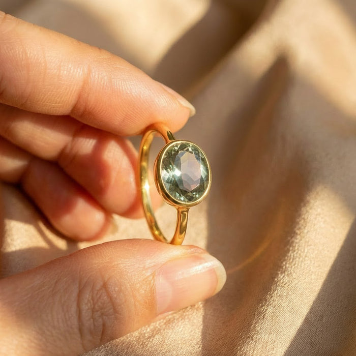 Handcrafted green amethyst February birthstone ring held close up, oval bezel set gemstone ring in gold, dainty minimalist jewelry with smooth polished finish