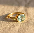 Green amethyst oval bezel set ring photographed at angle, February birthstone gemstone ring with smooth gold band, minimalist fine jewelry for women