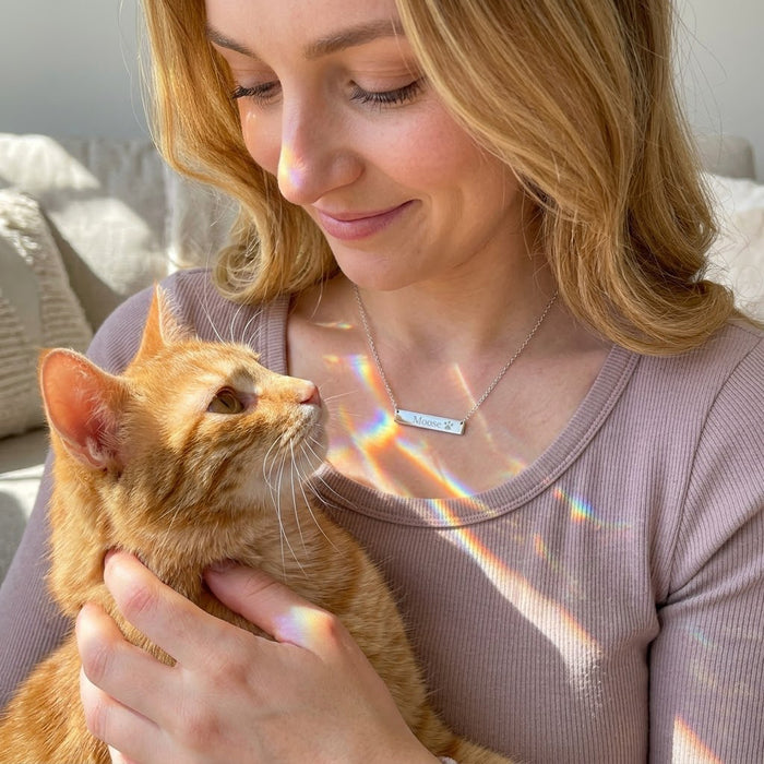 Woman wearing rose gold paw print bar necklace while holding orange cat, personalized cat memorial jewelry gift.