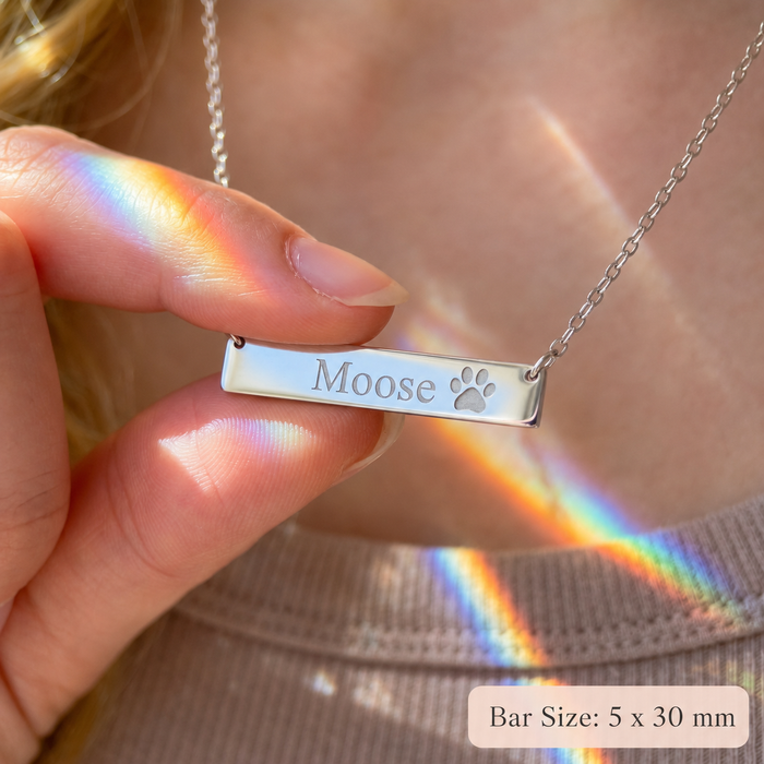 Close-up of silver paw print bar necklace engraved with pet name Moose, showing 5 x 30 mm bar pendant size.
