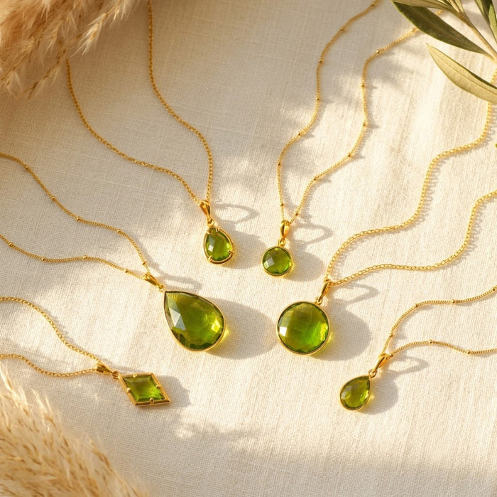 Peridot birthstone necklaces in yellow gold vermeil displayed on cream fabric in warm natural sunlight.