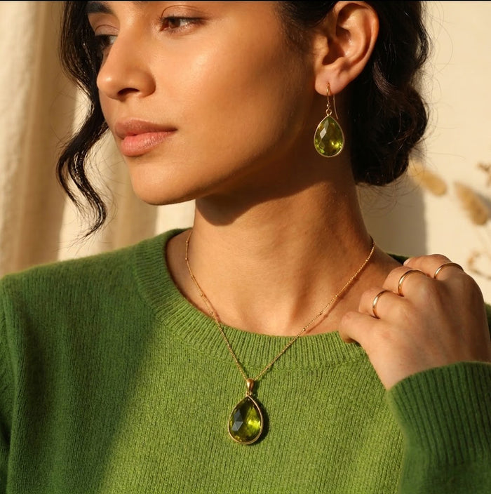 Model wearing a peridot teardrop necklace with a green sweater for an August birthstone jewelry look.