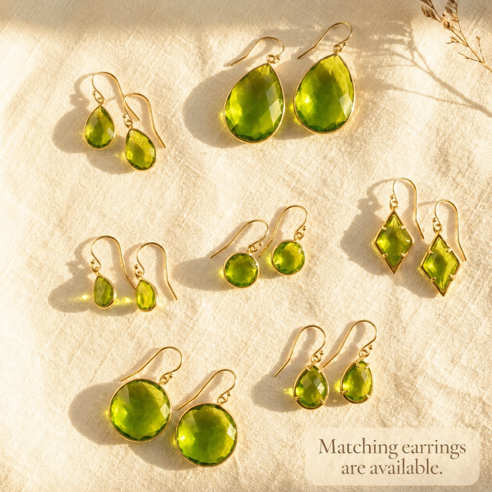 Matching peridot earrings and necklace set displayed on cream fabric in warm sunlight.