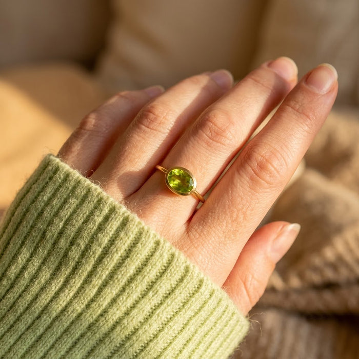 August birthstone peridot ring worn on a hand with a soft green sweater in natural light.