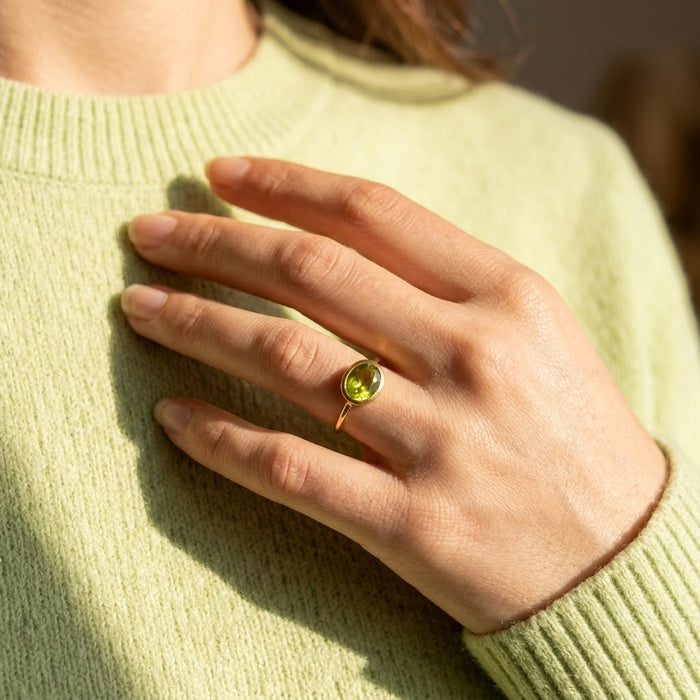Oval peridot gemstone ring shown on a model’s hand with a bright apple green August birthstone.