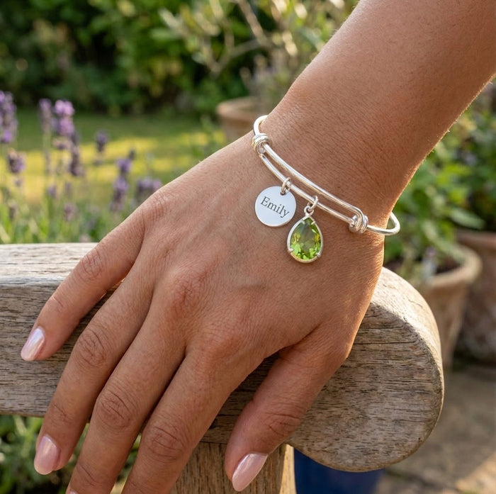 Custom birthstone bangle bracelet worn on wrist with engraved charm and green gemstone