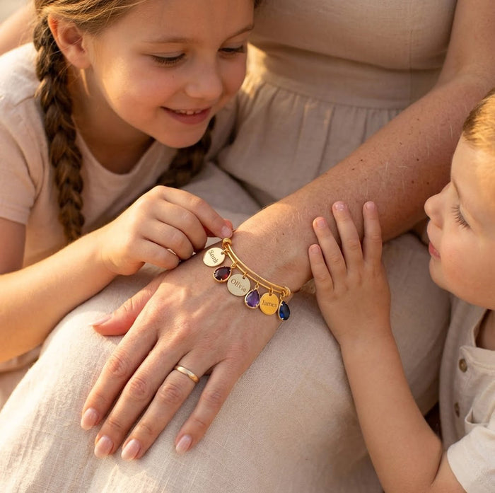 Mother wearing personalized birthstone bracelet while children hold her hand