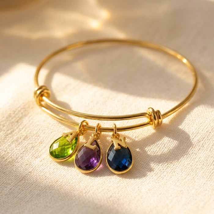 Personalized birthstone bangle bracelet with initial charms shown in warm sunlight.