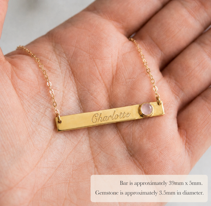 Custom name and birthstone bar necklace displayed in a hand with engraved personalization and gemstone accent.