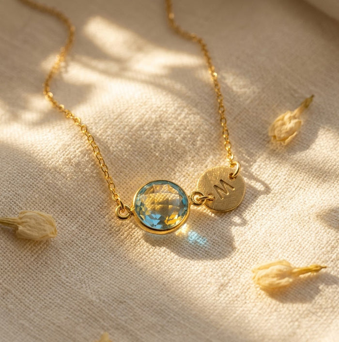 Gold blue topaz necklace with round faceted stone and brushed initial charm.