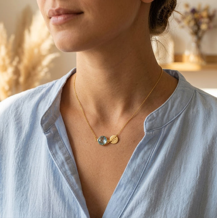 Personalized birthstone and initial necklace shown on a model with blue topaz charm.