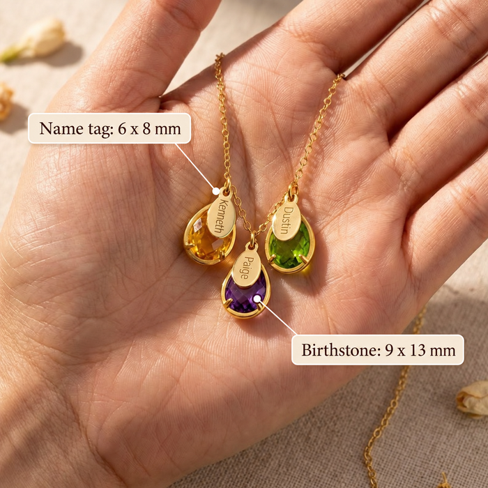 Close up of engraved oval name tags with teardrop birthstones in hand
