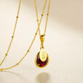 Personalized garnet January birthstone necklace with engraved oval name charm on gold chain.
