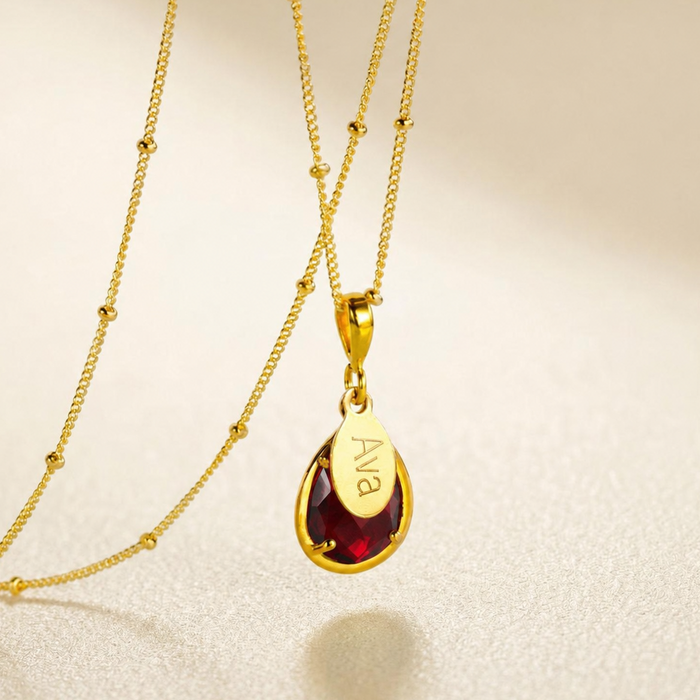Personalized garnet January birthstone necklace with engraved oval name charm on gold chain.