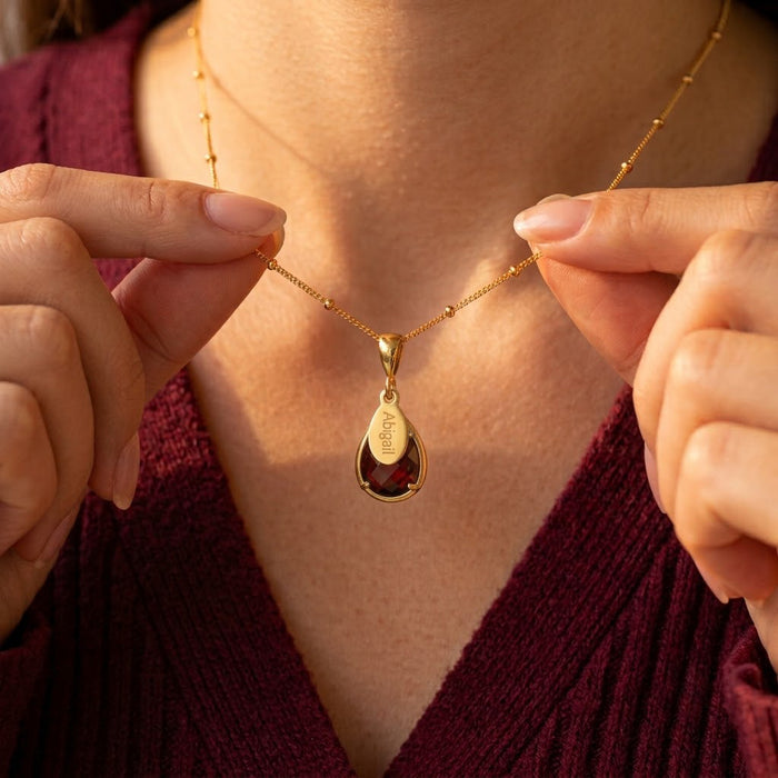 Garnet teardrop name necklace worn by a model in a burgundy top.
