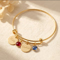Gold bangle bracelet with engraved disks in handwriting script and garnet and kyanite birthstones.