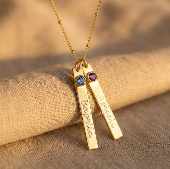 Custom name bar birthstone necklace with two engraved charms and gemstone accents on gold chain