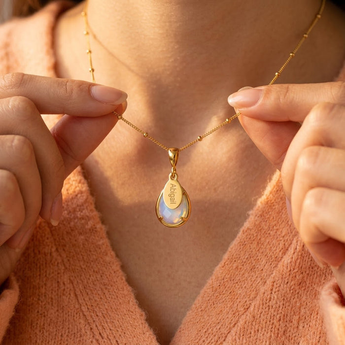 Opalite teardrop name necklace worn by a model in a peach sweater.