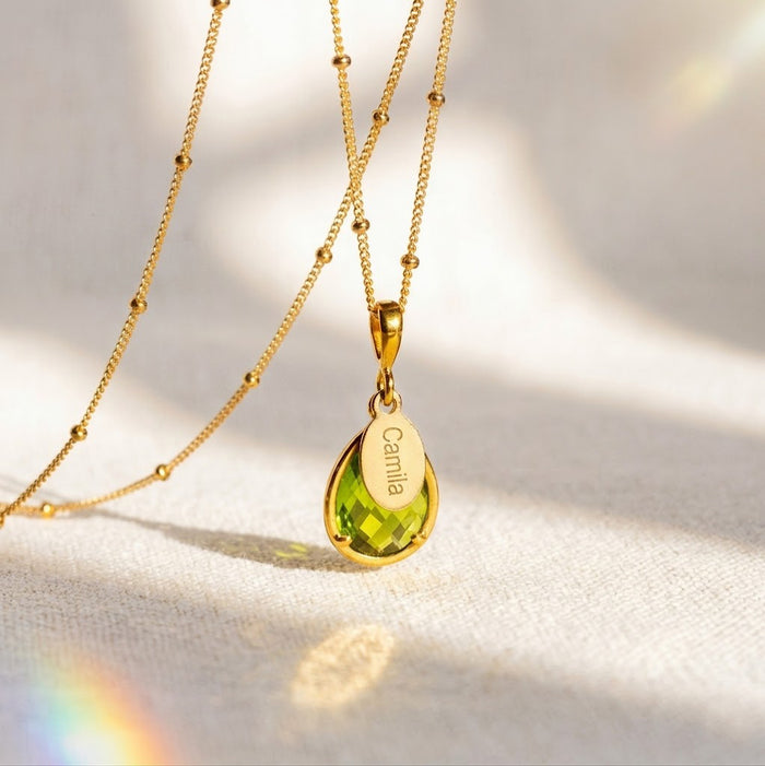 Personalized peridot necklace with engraved name tag on a gold chain, an August birthstone necklace with a green teardrop gemstone for a custom birthday gift.