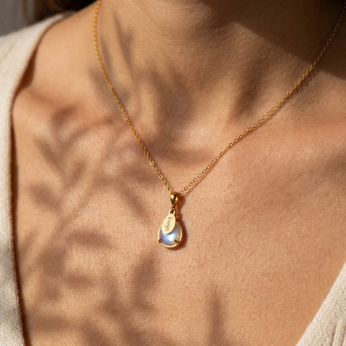 Model wearing dainty moonstone name necklace, showing small teardrop pendant and personalized oval charm on gold chain.