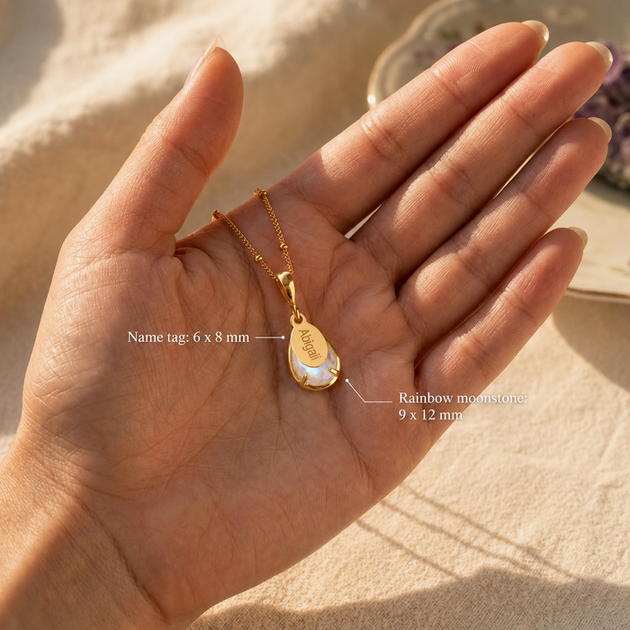 Rainbow moonstone necklace on palm with measurements showing 9 x 12 mm stone and 6 x 8 mm name tag.