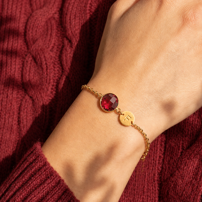 Ruby birthstone initial bracelet worn against a soft burgundy sweater