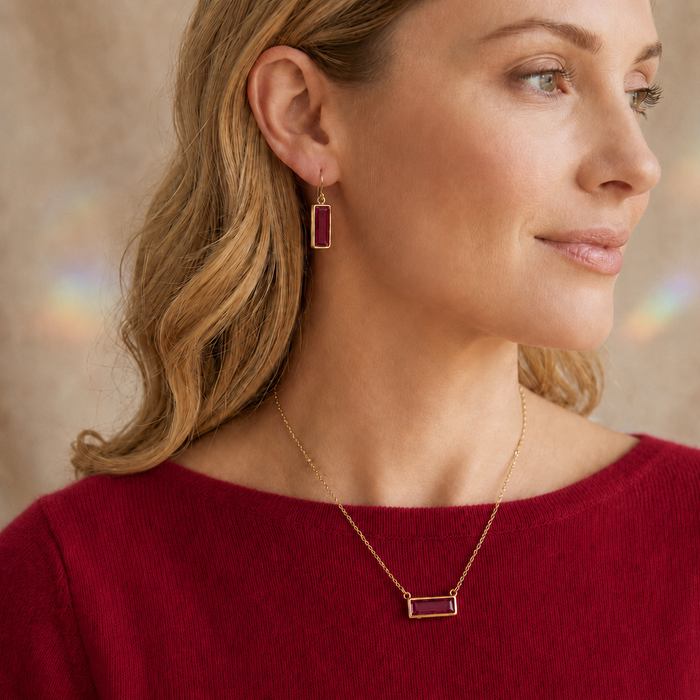 Model wearing a dainty ruby baguette birthstone necklace with matching ruby earrings.