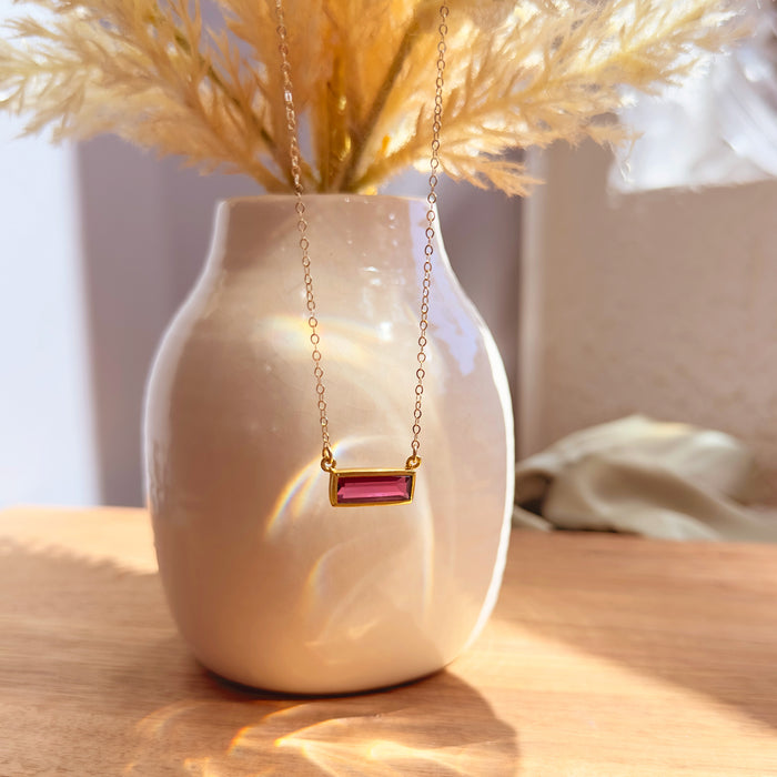 Ruby baguette necklace displayed on a cream vase with warm sunlight and dried floral styling.
