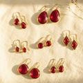 Ruby quartz earrings collection with multiple July birthstone earring styles shown on cream fabric in warm natural sunlight.