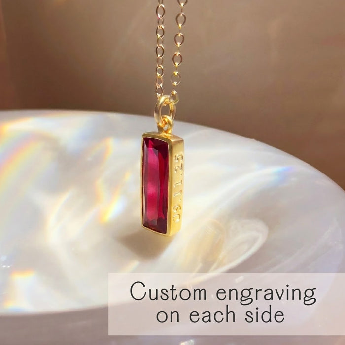 Ruby bar pendant necklace with custom engraving shown on a shell in golden sunlight.