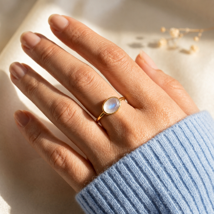 Model wearing stacked oval birthstone rings with a moonstone ring and other gemstone rings in gold.