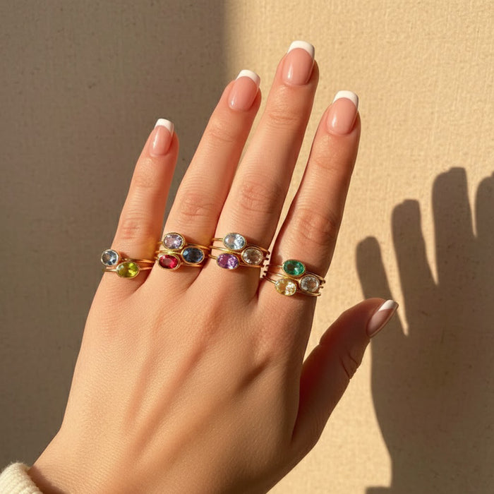 Hand wearing stacking birthstone rings including May Emerald, April Dimond Clear Quartz, September Sapphire in gold and silver, minimalist oval gemstone rings stacked on fingers, dainty birthstone jewelry for mom, wife, or girlfriend, personalized family birthstone rings perfect for everyday wear or gifting