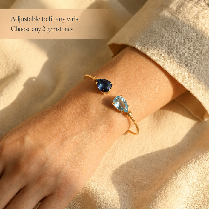 Adjustable birthstone cuff bracelet worn on wrist with two blue gemstones and text showing it fits any wrist size.