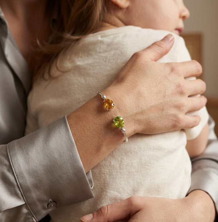 Personalized two birthstone bangle bracelet styled on wrist oh mom holding her child, a meaningful gift for mom, sister, or daughter.