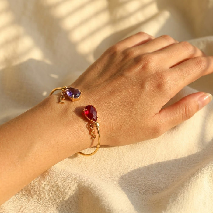 Personalized birthstone initial bangle bracelet worn on the wrist, a dainty gold bracelet customized with two gemstones and letter charms.