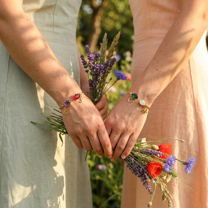 Bride wearing custom two birthstone initial bangle bracelet with colorful gemstones, a meaningful bridesmaid or wedding jewelry gift.