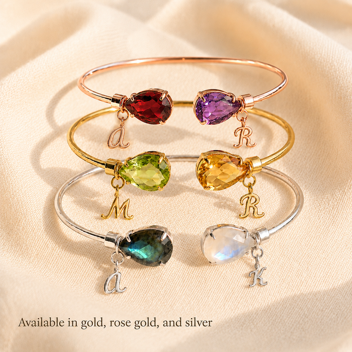 Three birthstone bangle bracelet with teardrop gemstones and initial charms, available in rose gold, gold and sterling silver for a personalized gift.