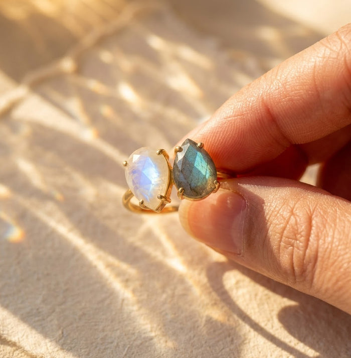 Close up of gold teardrop birthstone ring held between fingers in warm sunlight