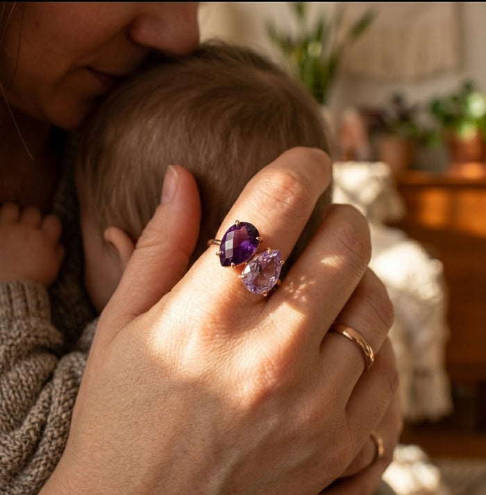 Double birthstone teardrop ring with purple stones worn on hand beside baby